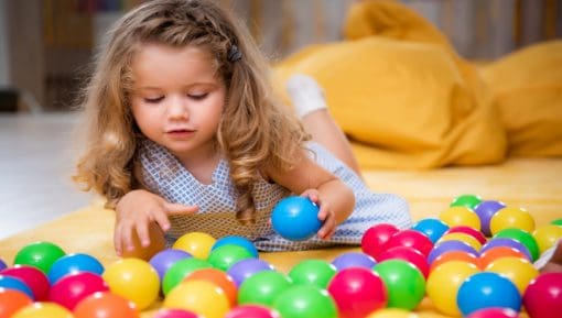 Child lying on carpet and playing with colorful balls